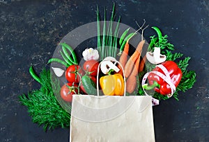 Paper bag with fresh vegetables on a dark background: tomato, zucchini, onion, lettuce, dill, pepper, cucumber, garlic