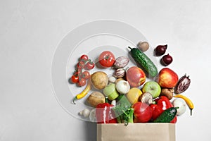 Paper bag with fresh vegetables and fruits on light background, flat lay.