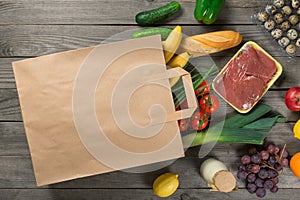 Paper bag full of different groceries on wooden background