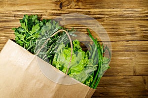 Paper bag with green onion, rosemary, lettuce leaves and parsley on wooden table. Top view. Healthy food and grocery shopping