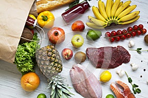 Paper bag of groceries on white wooden background, top view. Health food.