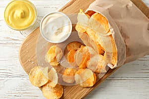 Paper bag of potato chips. Beer snacks, sauce on cutting board, on white wooden background, space for text