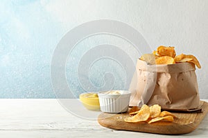 Paper bag of potato chips. Beer snacks, sauce on cutting board, on white wooden background