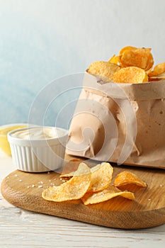 Paper bag of potato chips. Beer snacks, sauce on cutting board, on white wooden background, space for text