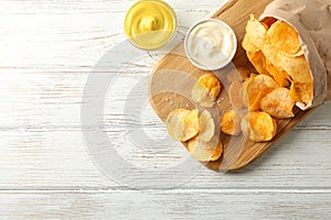 Paper bag of potato chips. Beer snacks, sauce on cutting board, on white wooden background, space for text
