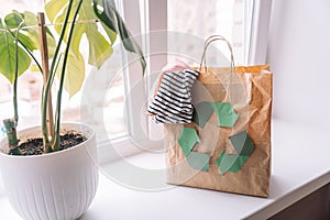 Paper bag with a recycling sign with old clothes on a windowsill with a flower
