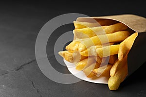Paper bag with tasty french fries on black table, closeup. Space for text