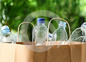 Paper bag with used plastic bottles against blurred background, closeup. Recycle concept