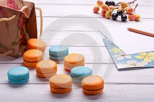 Paper bags with biscuits colorfool macaroons and postcard with pencil and envelope. Delicious French dessert on a white wooden bac photo