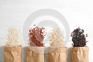 Paper bags with different types of rice on white wooden background, top view.