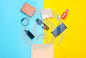 Paper bags and many purchases of gadgets and accessories on a colored background: sunglasses, smartphone, smart bracelet, powel