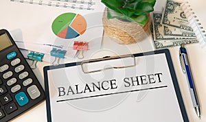 Paper with BALANCE SHEET on the table, calculator and money