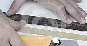 Paper being cut with razor blade and ruler close up.