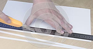 Paper being cut with razor blade and ruler close up.