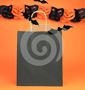 Paper black bag and decor for Halloween on orange background. Halloween shopping concept. Mock up. Copy space. Selective focus