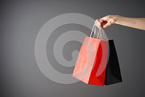Paper black and red bag, eco packaging in a female hand on a gray background. Space for text