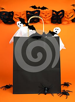 Paper black shopping bag and decor for Halloween on orange bright background. Mock up. Halloween shopping and sale concept. Place