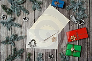 Paper blank, envelope, gift boxes, fir branches, cones, wooden decorative toys, snowflakes on a wooden background. Christmas, win