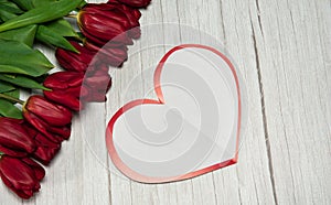 Paper blank in the form of a heart and a spring bouquet of red tulips on a light wooden background.