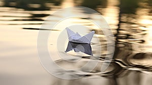 A paper boat is floating on the waves in the water at a beautiful sunset. Origami ship Sailing. The concept of a dream