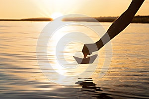 The paper boat goes on a big voyage at sunset, the boy`s hand launches the origami ship on the water