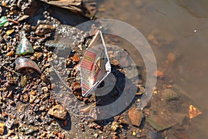A paper boat, a little boat made of an old newspaper, floats down the drain and is washed up on the bank of a muddy stream, away f