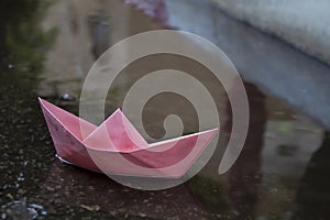 Paper boat, Origami ship, floats in a puddle formed by the pouring rain. Photo idea: floods, autumn or winter weather