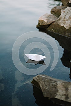 paper boat sailing on blue water surface near stones
