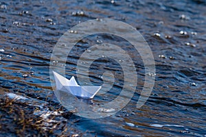 A paper boat on a turbulent stream of water struggles with the flow. Small paper boat is flowing along river