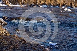 A paper boat on a turbulent stream of water struggles with the flow. Small paper boat is flowing along river