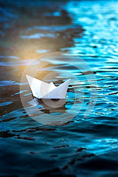 Paper boat in the water, white origami ship floats on the waves, vertical frame