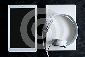 Paper book, ebook and audio book format on a black wooden table. Top down view of a desktop with empty copy space.