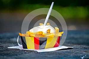 Paper box in colors of Belgian flag with fried potato frit chips and mayonnaise sauÑe