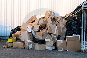 Paper boxes next to a garbage bin. Stack of paper waste outdoor in the city. Paper recycling, nobody