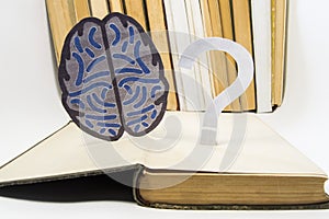 Paper brain silhouette and question mark is over old open medical book. Photo to refer issues and questions in study of brain, as