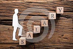 Paper Businessman Climbing Salary Block Ladder On Wood