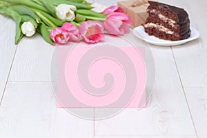 Paper card, bouquet of pink tulips, chocolate cake. pressent box on white wooden background. Copy space, close up. Mother`s, women