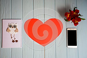 Paper card in form of red heart with copy space with smartphone on desk