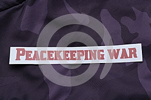 Paper card with phrase Peacekeeping War on color fabric, top view