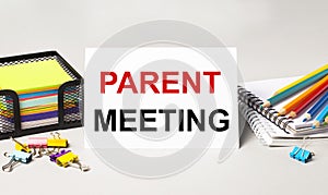 A paper card with the text PARENT MEETING, multi-colored pencils, stickers and paper clips on the desktop