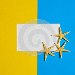 Paper card with three sea stars on blue and yellow paper background. Mock up, flat lay, copy space, top view. Summer vacation