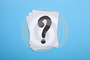 Paper cards with question marks on blue background. Pile of question marks, top view