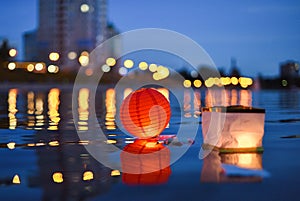 Paper Chinese lanterns floating in river with city lights reflections