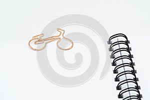 Paper clip in shape of bike on spiral notebook on white background