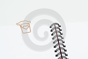 Paper clip in shape of coffee cup on spiral notebook on white background