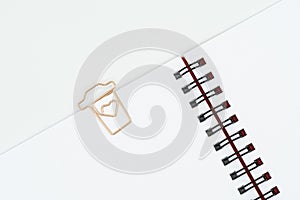 Paper clip in shape of coffee cup on spiral notebook on white background