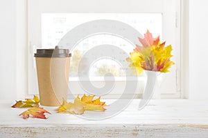 Paper coffee cup and autumn leaves on table with space
