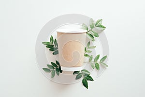 Paper container cup of coffee to go with green leaves on white background. Flat lay, top view