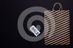 Paper craft bag with black stripes and sale tag on black background. Black Friday concept