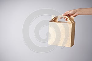 Paper craft bag, eco packaging in a female hand on a gray background, place for text